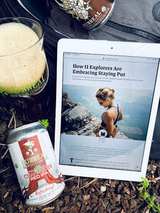 Can of Surreal Non-Alcoholic Red IPA next to an IPA displaying an article about Explorers staying put during Covid epidemic. 